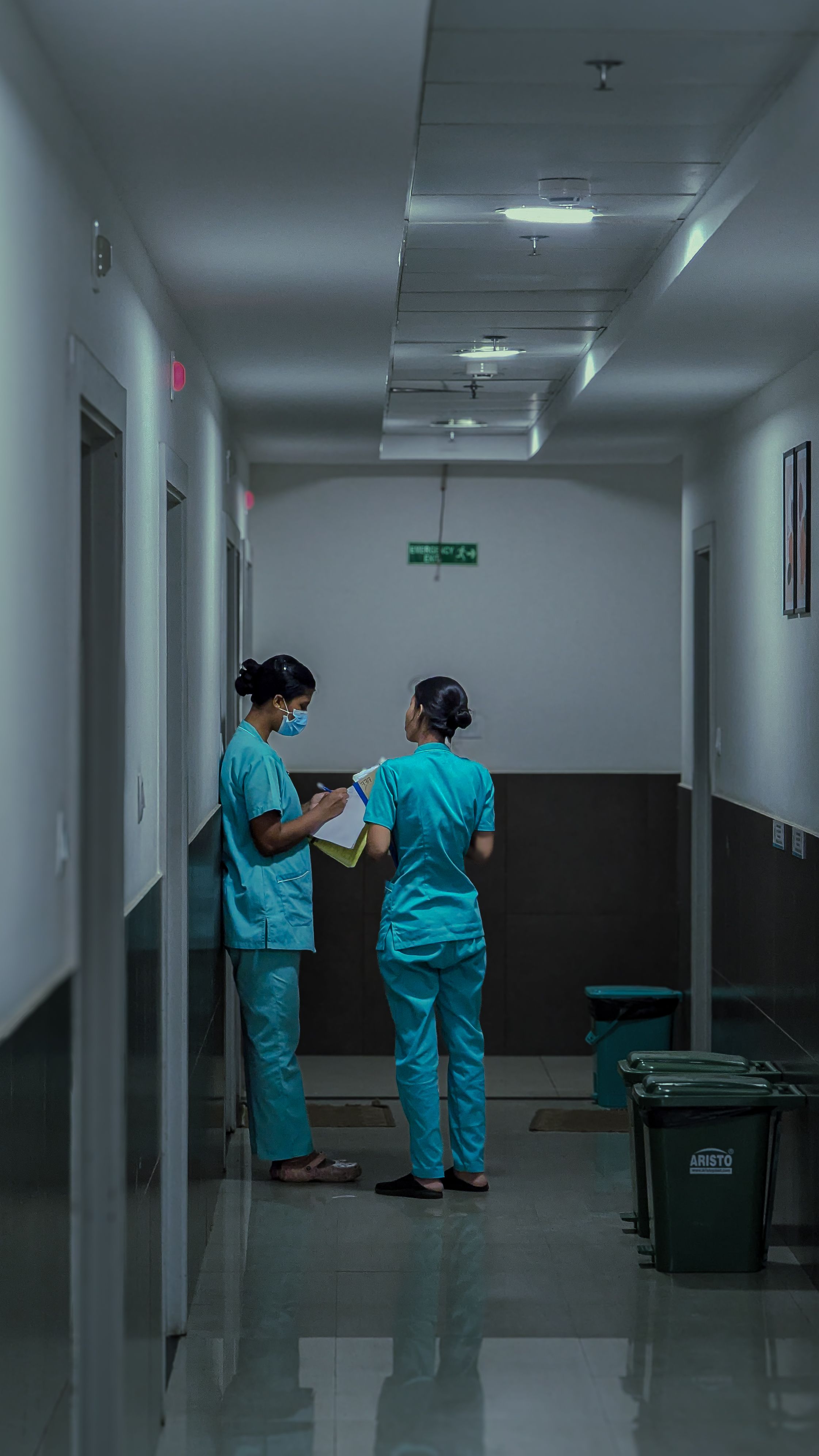 Two care professionals in scrubs reviewing patient notes together in a care setting corridor