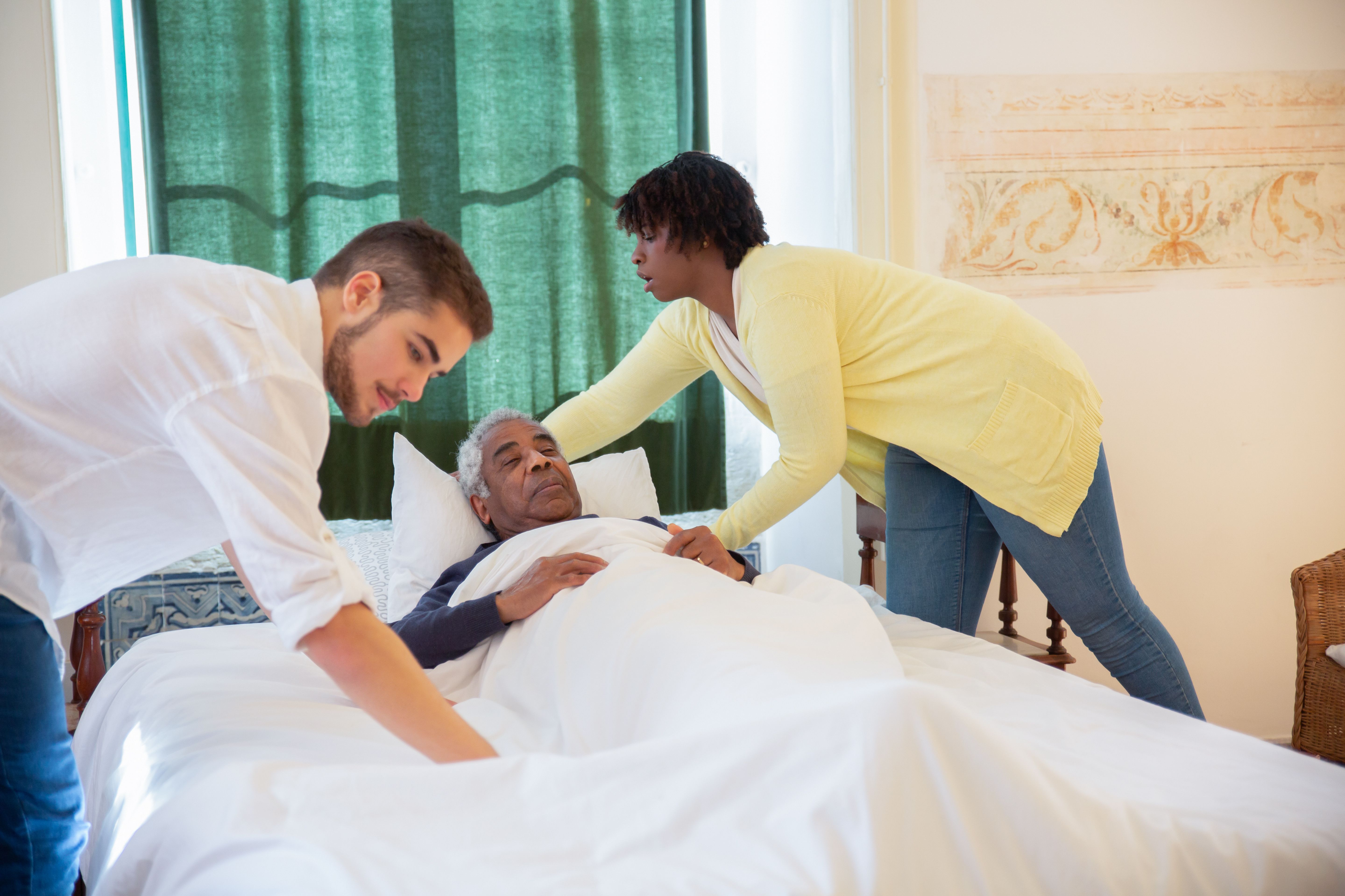Two care professionals working together to support a person at their bedside