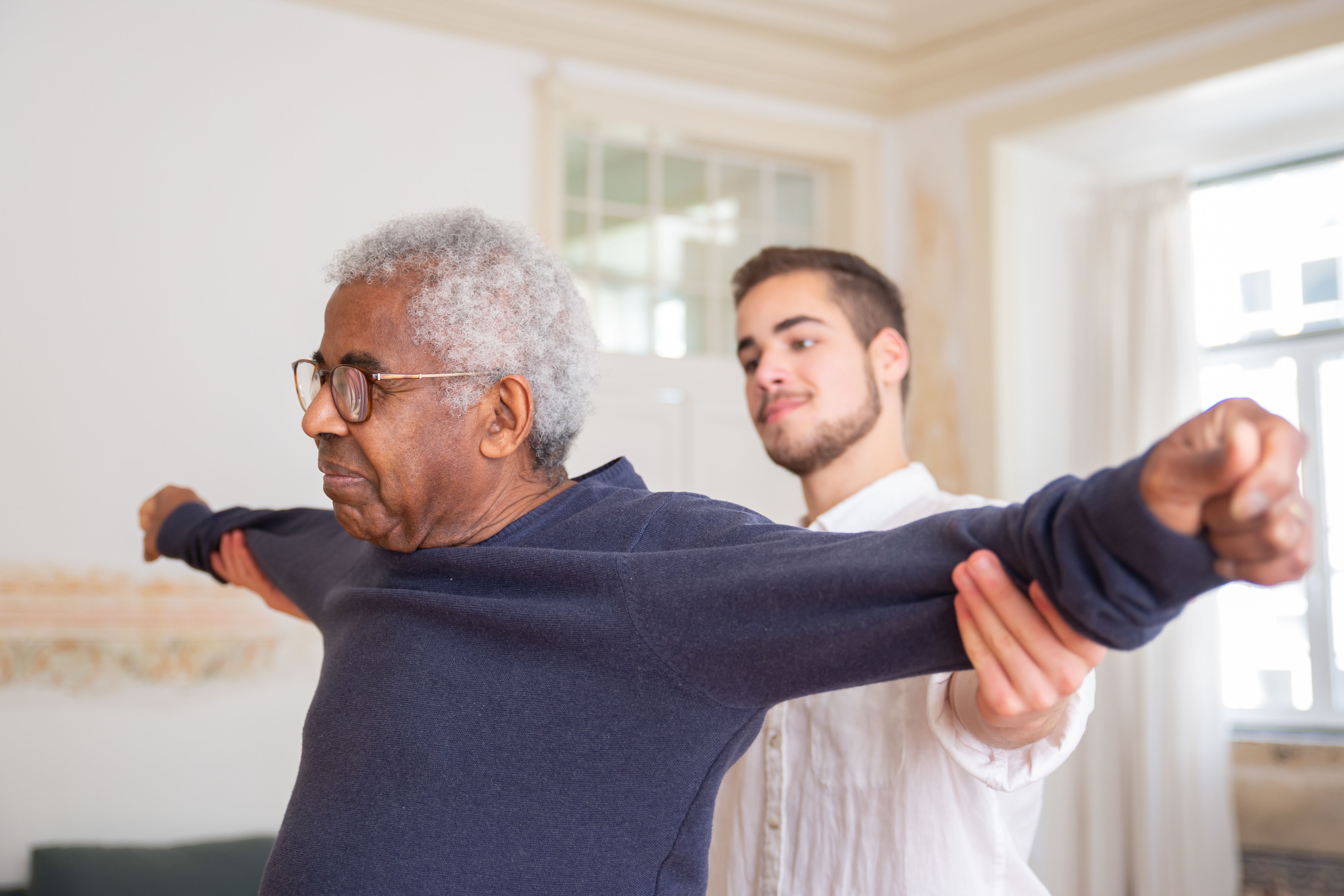 A support worker guiding an older man through a supervised exercise